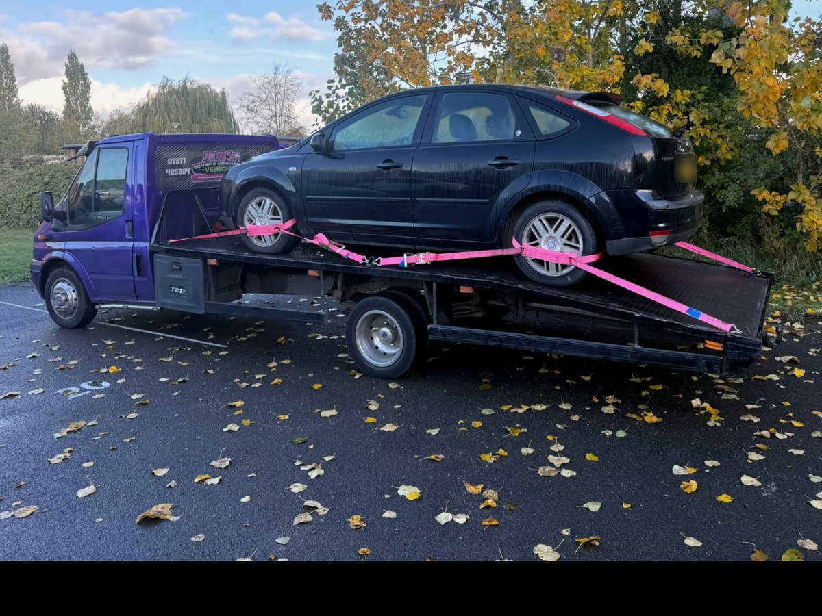 A black hatchback secured on BB's flatbed on an autumn day